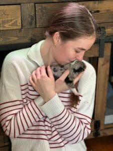 a woman kissing a toy australian shepherd puppy